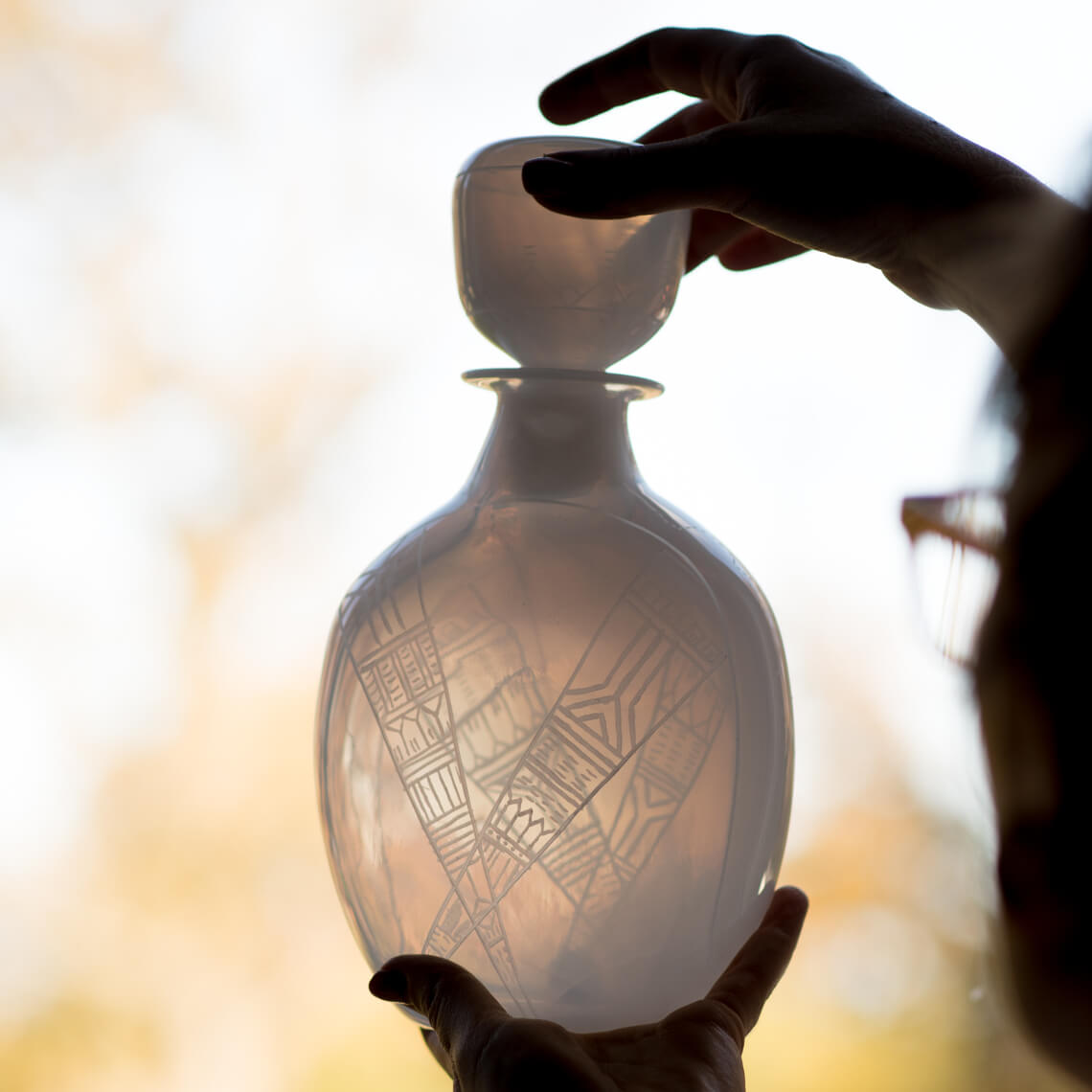 Translucent white glass decanter being held up to the light. The glass is engraved with geometric patterns